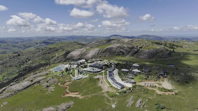 Drone orbits to the left in ultra wide shot high over mountain resort on a sunny day at Sibebe Rock near Mbabane, Eswatini