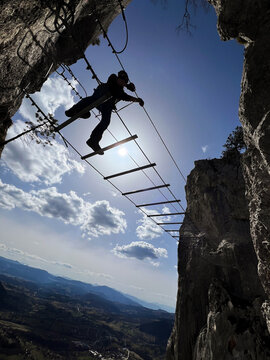 Man crossing a ladder suspension bridge on a via ferrata route over a deep mountain gorge