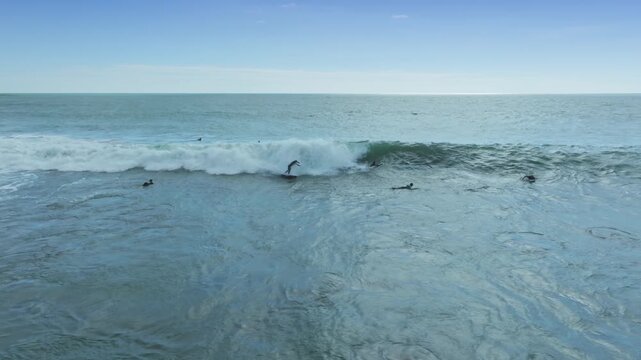 Surfers paddle in the turquoise waters off the coast of Raglan, New Zealand, enjoying the waves on a sunny day.