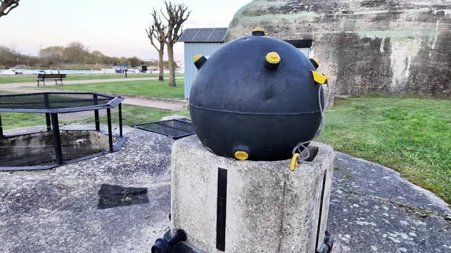 Close-up static shot of a historic black naval mine displayed on a concrete pedestal.