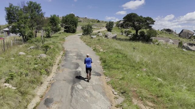 Drone flies low over lone hiker and continues to top of trail to reveal landscape on a sunny day at Sibebe Rock near Mbabane, Eswatini