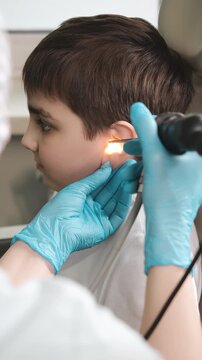 Doctor examining child ear with otoscope in clinic, pediatric healthcare and ear infection diagnostics in medical setting.