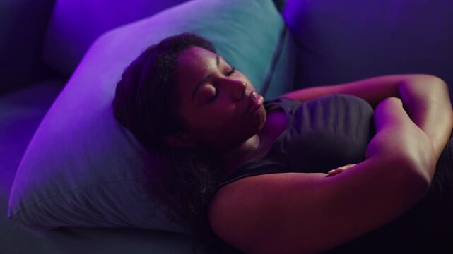 African American woman lying on couch with arms crossed looking down with tense expression reflecting on problem feeling upset and mentally preoccupied in quiet indoor space