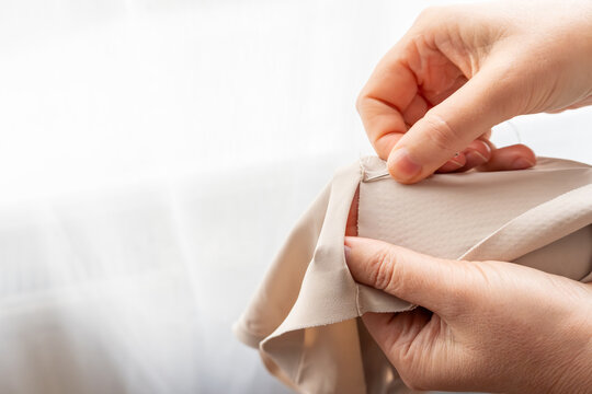 Woman darning a beige clothes by hand with needle and patch fabric