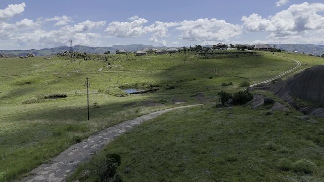 Drone starts low and flies over two hikers making their way to a mountain resort as drone flies up and over resort to show picturesque views on a sunny day at Sibebe Rock near Mbabane, Eswatini
