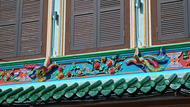 Shophouse facade with ceramic phoenix and floral reliefs, traditional green roof tiles and wooden shutters in Melaka, Malaysia, heritage architecture documentary .