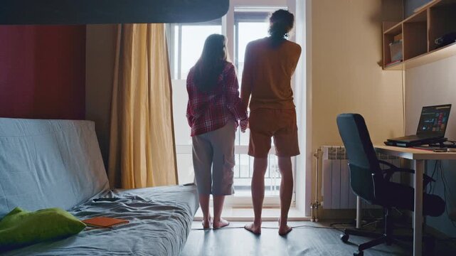 Silhouette of a young couple hugging and holding hands while looking out the window of their room