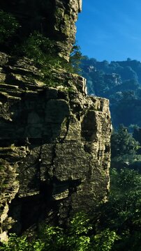 Towering rock cliffs emerge from lush greenery under a clear blue sky. Tranquility reigns in this stunning natural setting, inviting adventure and exploration.