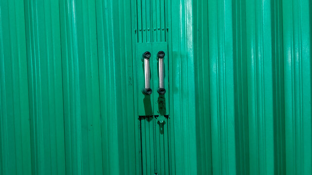 Close-up front view of a green corrugated metal door featuring stainless steel handles in a perfectly symmetrical composition. The vibrant teal surface creates a strong industrial
