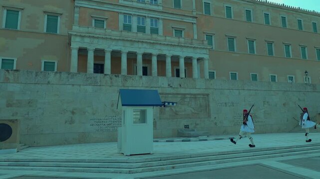 Two Greek Evzones guards perform synchronized ceremonial movements in front of the Hellenic Parliament and the Tomb of the Unknown Soldier in Athens.