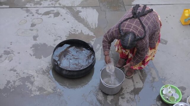 A cholita carrying water in a pot using a transparent plastic pitcher in a courtyard.&nbsp;