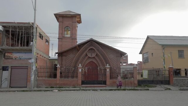 The Church of Batallas, a small Christian church in a small town. A cholita walks in front of the church on a cloudy day.