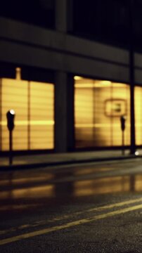 Soft amber light spills from windows, illuminating the wet pavement. Streetlights stand guard on a quiet urban street, hinting at stories from a serene night.