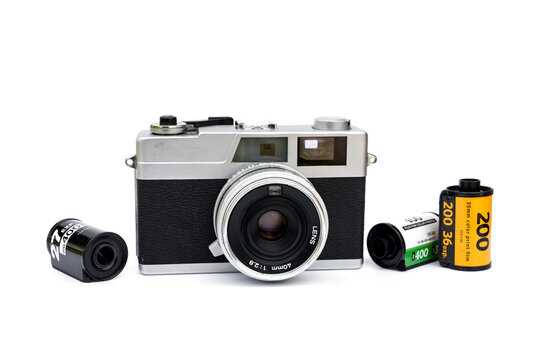 Collectibles vintage retro photography analog hobby concepts. Silver rangefinder camera with 40mm lens with black, yellow, and green rolls of 35mm color print film isolated on white background.