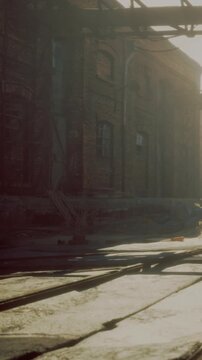 Dusty, worn tracks lead through a forgotten industrial area, where golden sunlight pierces through the structures. Shadows dance as the day gently fades into night, revealing a sense of nostalgia.
