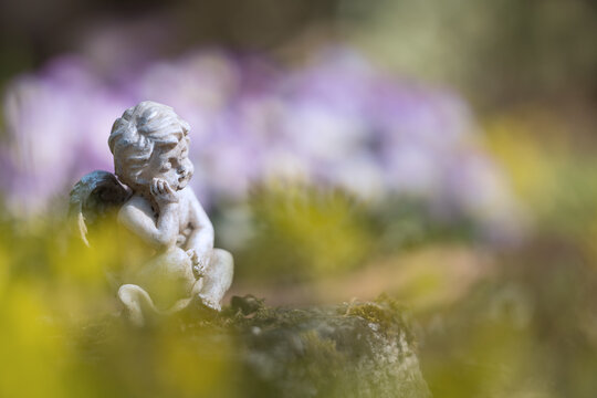Leuchtende Fr&uuml;hlingsfarben im Blumenbeet mit kleiner Engelsfigur am Grab, soft Hintergrund