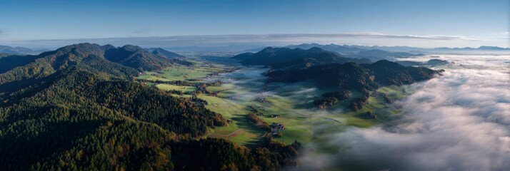 Fototapeta premium Panoramic ridge and valley aerial view with morning fog rolling through green pastures and forested hills under clear blue sky wide natural landscape