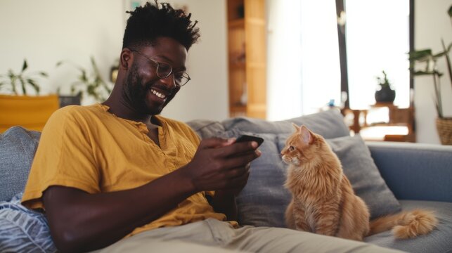 Man Sitting on Couch with Cat, Looking at Phone