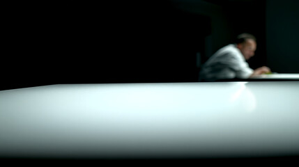 Fototapeta premium Blurred man in a white shirt working at a table in a dark room.
