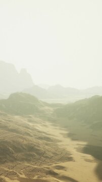 A serene desert scene unfolds with gentle golden sands and soft, rolling hills. In the distance, hazy mountains rise, illuminated by the warm glow of dawn. Nature showcases its beauty.