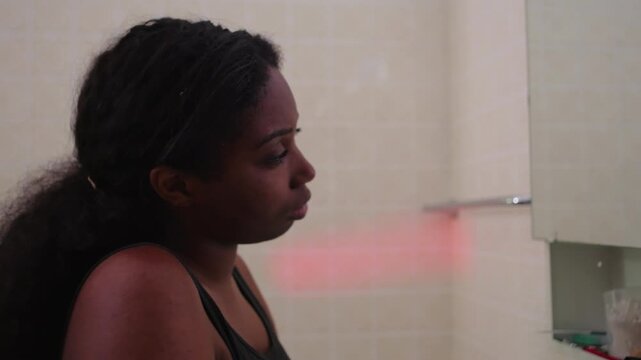 African American woman staring at mirror as camera pans from reflection to face and back, conveying inner thoughts, self reflection, quiet contemplation, and emotional introspection