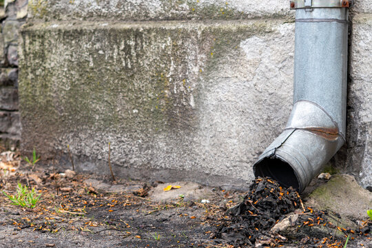 Clogged downspout full of dry leaves and debris against an old concrete wall. Gutter system maintenance problem, autumn cleaning, dirty metal drainage pipe needing repair and clearing.