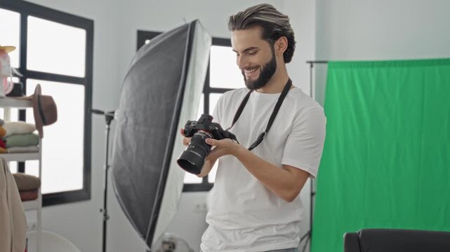Man holding camera and checking settings with hands in studio, smiling near green screen and softbox; happy creative workflow.