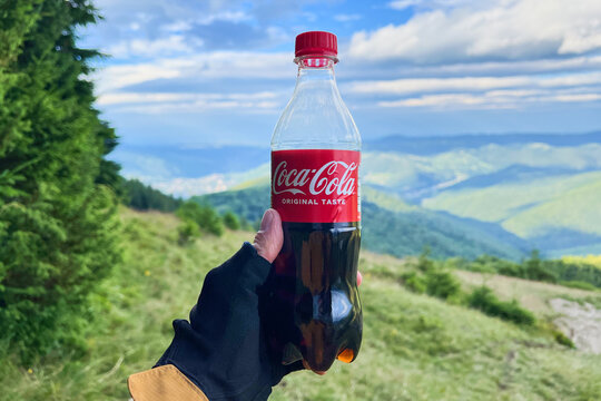 First person view of Coca-Cola bottle with scenic hills and cloudy sky in background