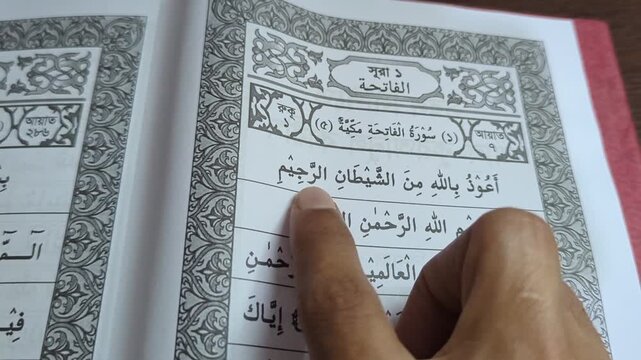 Religious text reading process with finger pointing at verses on white paper background in close up view showing detailed script of traditional literature book for educational purpose in day.