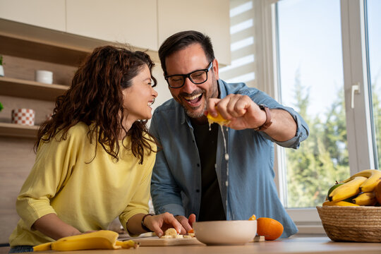 Happy couple cooking fruit salad at home, husband squeezing lemon juice