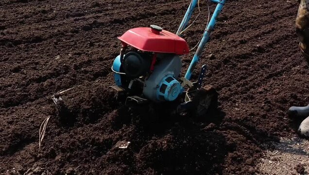 A man plows the land with a motor cultivator in a field.