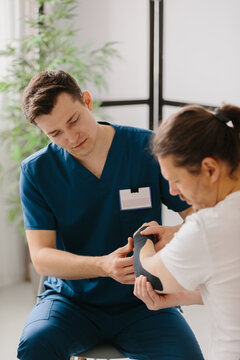 Physician applying kinesiology tape to a patient's arm for treatment.