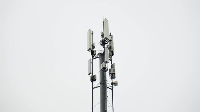 A tall cell tower rises against a gray sky. It has multiple antennas on top
