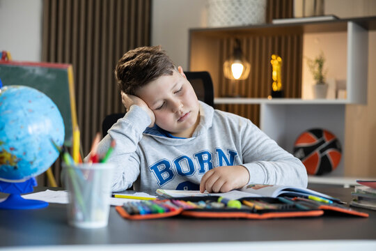 Young boy feeling tired and stressed, sleeping at his desk while studying, experiencing boredom from school education