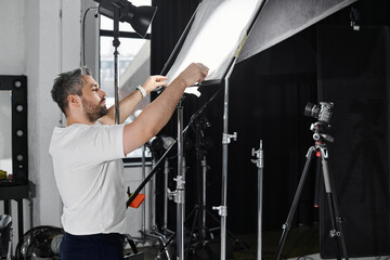 Obraz premium Professional man adjusts lighting equipment while preparing for a creative shoot in a studio