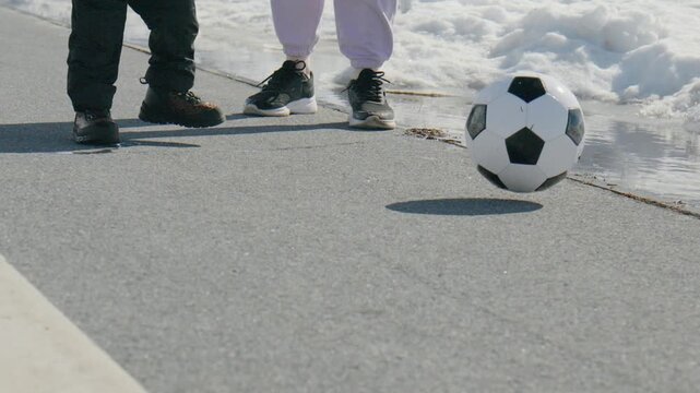 Child practices soccer skills on a street with a black and white ball while wearing winter clothing
