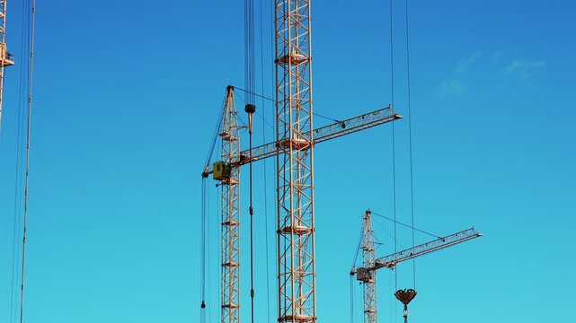 Cranes are lifting materials at a construction site in the city. The building work is ongoing under bright blue skies