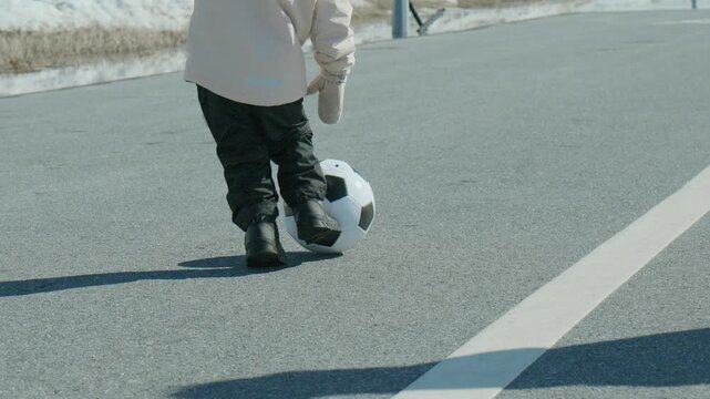 Kids practice football on a cold day with snow on the ground near a paved road and an adult supporting them