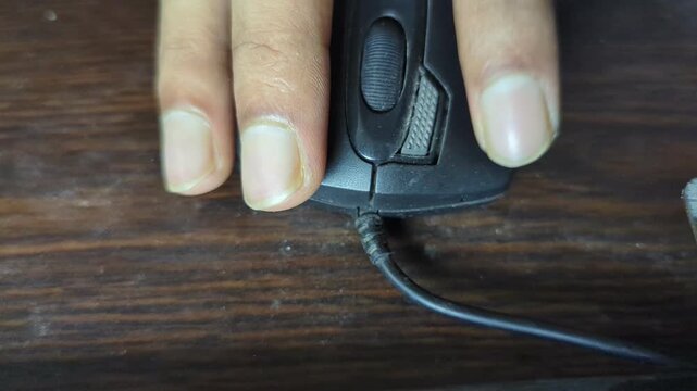 Person using black computer mouse on wooden table surface close up view with hand movements and red led light illumination during scrolling activity dynamic tech footage for office work theme.