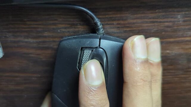 Close up footage of finger pressing computer mouse buttons for scrolling website or clicking links, technology detail shot.