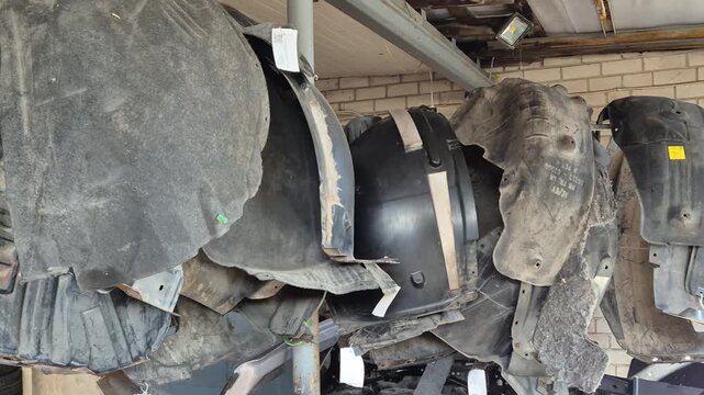 Used car fender liners hanging in auto salvage yard, dirty worn plastic parts, dismantling process and spare parts recycling concept