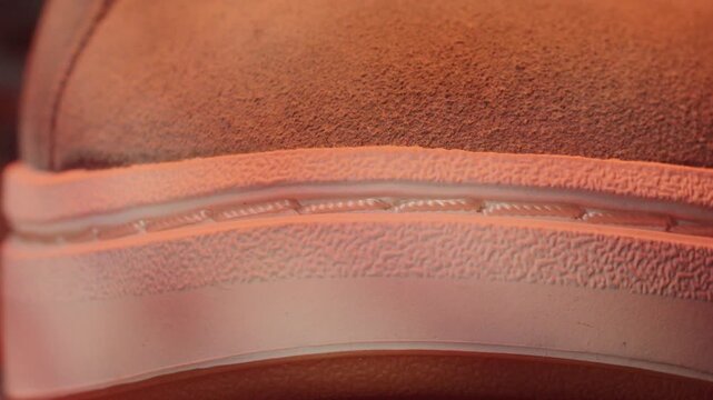 Sneaker sole stitching closeup showing welt and rubber midsole, textured suede upper and seam detail under warm studio light, product inspection angle