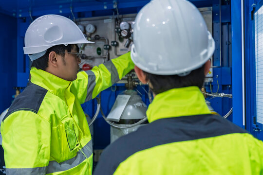 Professional engineers inspecting industrial gas control system and high pressure cylinders in technical laboratory. Focused on safety compliance, energy management, and maintenance maintenance.