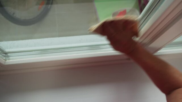 A person stands near a window in a home. They use a squeegee to clean the glass