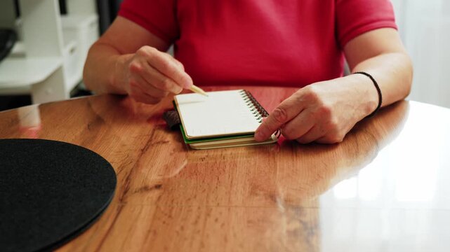 Hands write in a sketchbook on a wooden table during a creative moment at home in the afternoon