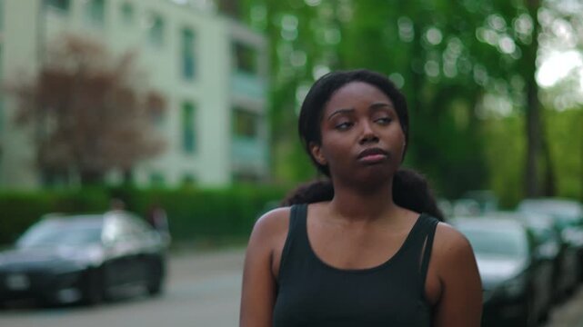 African American woman walking forward along residential street with pensive and introspective expression while camera tracks her movement creating reflective and contemplative