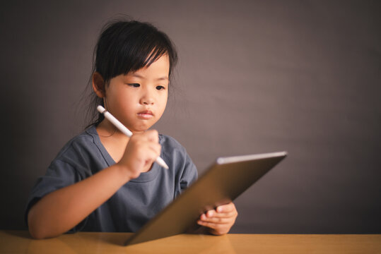 Little Asian girl smiling while using tablet and stylus for remote learning at home