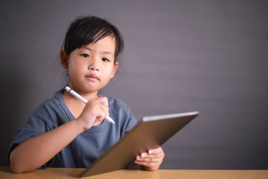 Little Asian girl smiling while using tablet and stylus for remote learning at home