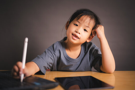 Little Asian girl smiling while using tablet and stylus for remote learning at home