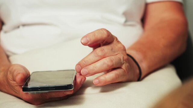 A person is sitting in a chair at home, holding a mobile phone in one hand